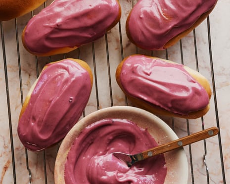 Oblong finger buns with purple blackcurrant glaze sit on a wire rack beside a bowl of icing