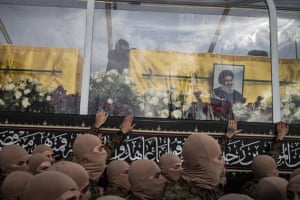 People with faces covered, holding hands up to where the coffins sit behind glass