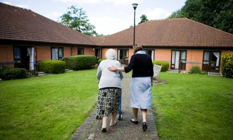 A care worker guides an older woman along a path