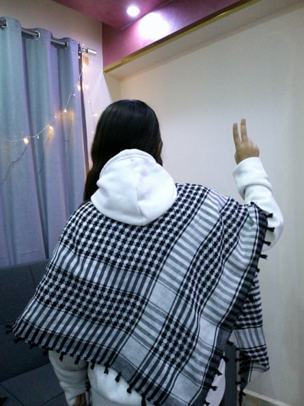 Girl in keffiyah with her back to the camera makes a peace sign