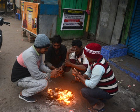 Young men gather round a small fire burning on the street to warm themselves