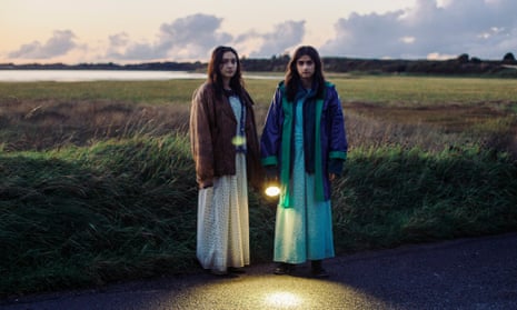 Two girls wearing long skirts standing by a roadside holding a torch in September Says.