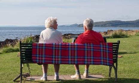 An elderly couple sitting on a bench at the waters edge.
