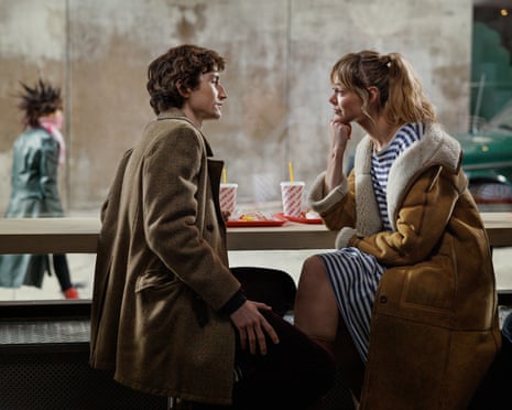 A young man and woman sitting at the window of a cafe with drinks in cups with straws