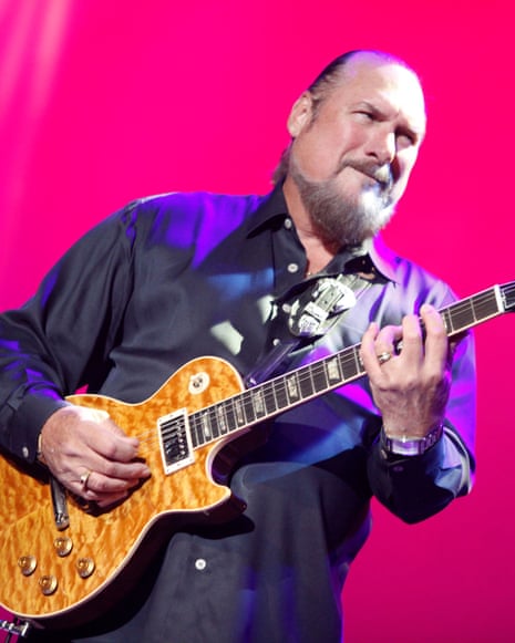person wearing button-down looks up while holding guitar