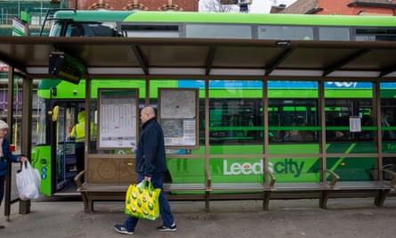 A green Leeds City doubledecker bus seen through the glass of a bus shelter
