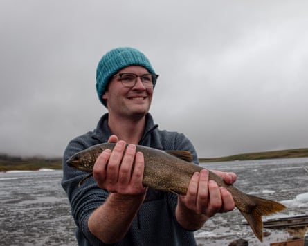 A man standing in a lake while wearing a bobble hat holding up a big fish with both hands A man standing in a lake while wearing a bobble hat holding up a big fish with both hands