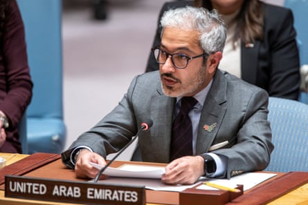 A bearded Arab man in a suit sits at a desk in a conference room