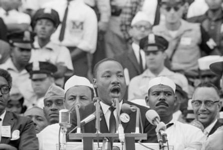 Martin Luther King speaks into a microphone as people watch behind him