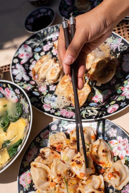 A hand holding a pair of black chopsticks and grabbing a boiled dumpling drizzled with a spicy dressing.
