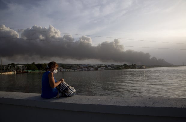 Ένας κάτοικος κάθεται στον θαλάσσιο τοίχο του Μαλεκόν καθώς καπνός υψώνεται στο βάθος από τη φωτιά.