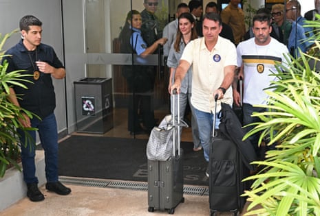 Flavio Bolsonaro walks outside building with his luggage as a crowd looks on