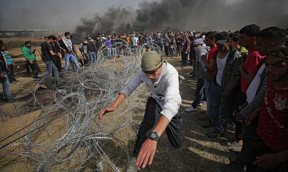 A protester pulls a barbed wire fence near the border with Israel. There are clouds of black smoke in the background