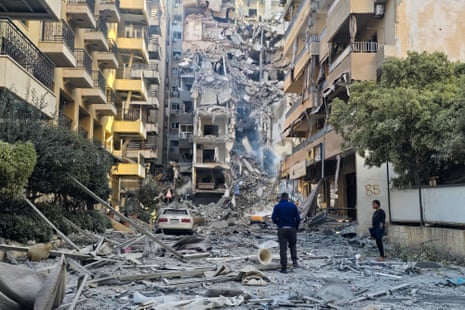 A man looks at a heavily damaged building at the end of a narrow street.
