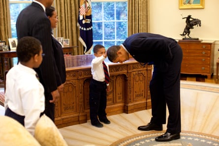 President Barack Obama bends over so the son of a White House staff member can pat his head during a visit to the Oval Office in 2009.