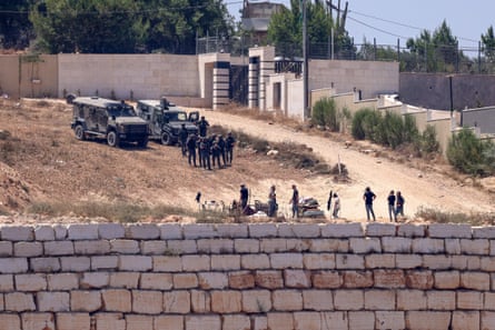 Israeli soldiers stand guard next to settlers in front of Palestinian houses