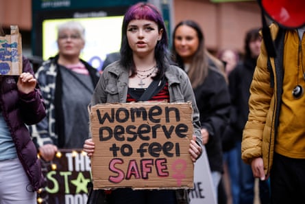 Woman with pink hair holds up a placard saying, ‘Women deserve to be safe’.