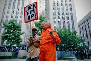 A person wearing an orange jumpsuit and a mask of former US president Donald Trump’s face holds a sign reading “lock him up!” outside the courthouse.