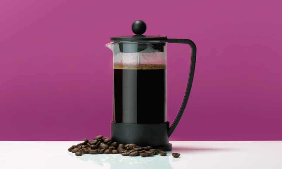 French press coffee pot on a table with coffee beans against a pink background