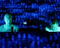 Overmono duo perform at electronic music equipment under blue stage lighting