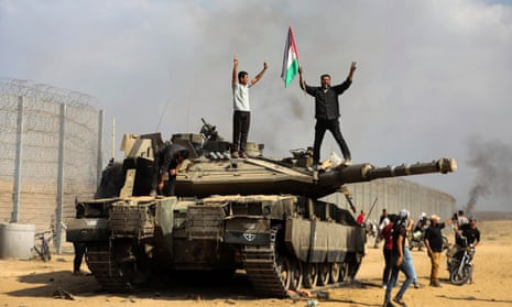 A photograph by Yousef Masoud showing Palestinians standing on and around a destroyed Israeli tank on the Israeli side of the Gaza border on 7 October.