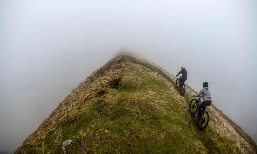 Two women ride mountain bikes along a ridge in the Brecon Beacons