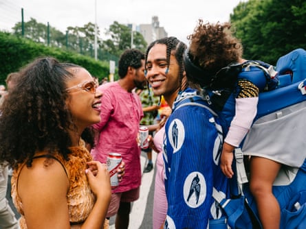 A woman talks and laughs with a man who has a young child sleeping in a carrier on his back