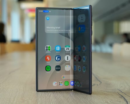 A Samsung Galaxy Z Fold 8 Ultra stood up on a wooden table partially folded showing the home screen on its tablet display.