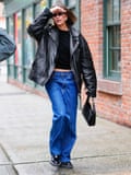 Hayley Bieber wearing black leather jacket and blue wide leg jeans.