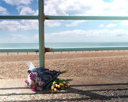 A bouquet of flowers is left on a pavement, with Brighton beach and the sea in the background