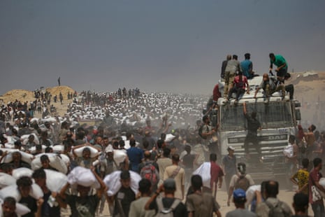 Internally displaced Palestinian people carry bags of flour near a food distribution point in Zikim, in the northern Gaza Strip on 27 July 2025.