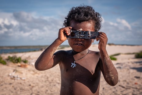 A small girl on a beach peers through holes in a bit of plastic