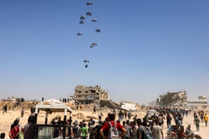 People gather as a C-130 Hercules military transport aircraft drops humanitarian aid