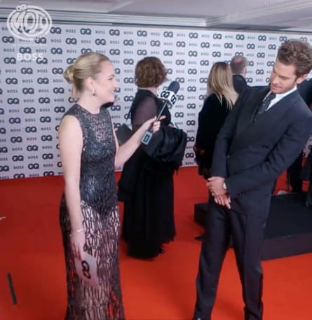 Amelia Dimoldenberg holding a microphone towards Andrew Garfield as he looks at her partly transparent dress.