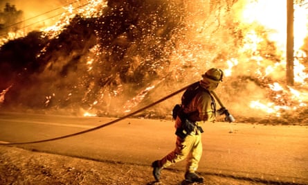 A firefighter carries a hose closer to flames throwing embers in Filmore, California