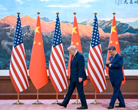 two men walk across a stage featuring a line of US and Chinese flags