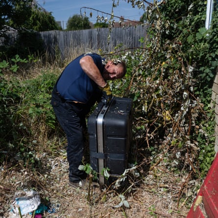 He grapples with the large black case as a strand of ivy tickles his head