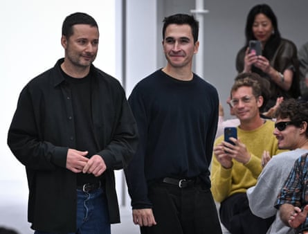 Two men dressed in black being cheered on runway at fashion show.