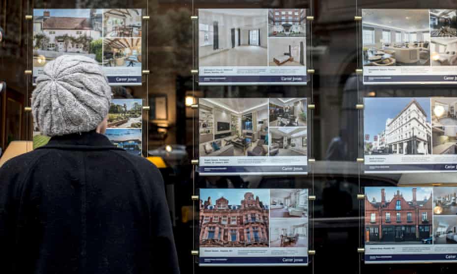 a woman looks at homes for sale in an estate agent window