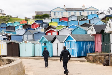 Two people walking along a path with beach huts