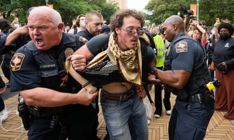 Police officers arrest detain a man with protesters in the background