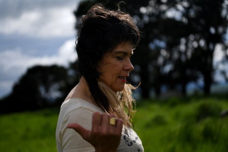 A portrait from the side of Judith Crispin as she walks through a grassy field. She gestures behind her with her thumb