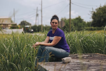 a woman in a purple shirt and blue jeans its on a concrete block in a grassy field