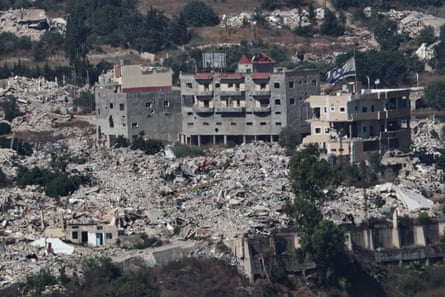 A large Israeli flag waves atop a destroyed house, as other destroyed buildings and vast amounts of rubble surround it