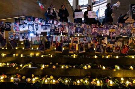 Rows of candles and flowers in front of dozens of memorial photographs of Iranian people.