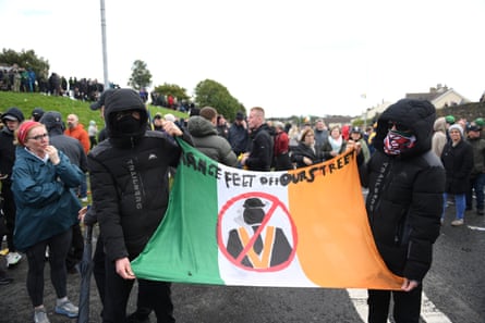 Protesters hold an Irish flag with the words 'Orange feet off our street' painted on it