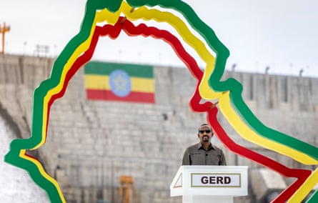 Abiy Ahmed speaks at a lectern set up in front of the dam. A decorative structure in the shape of the country of Ethiopia, and in the colours of its flag, surrounds him