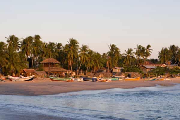 Arugam Bay beach with boats, thatched roof buildings and palm trees at first light.