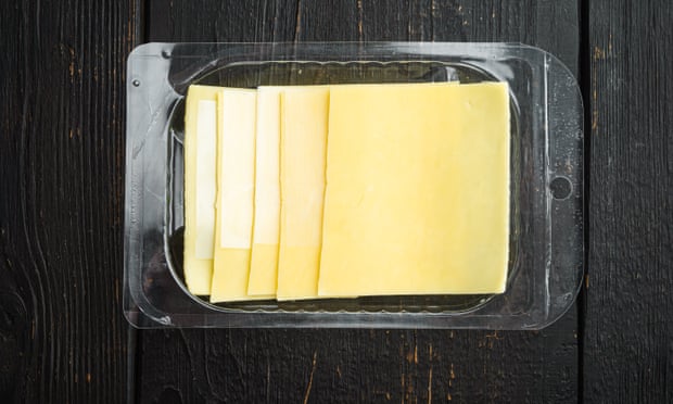 Yellow cheese slices of cheddar, in plastic pack, on black wooden table background, top view flat lay