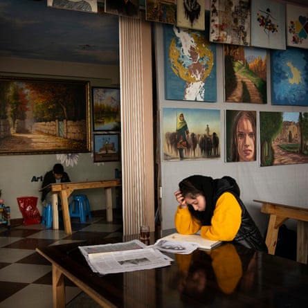 A girl in a headscarf sits at a desk with a drawing pad. Behind her can be seen works of art on the wall
